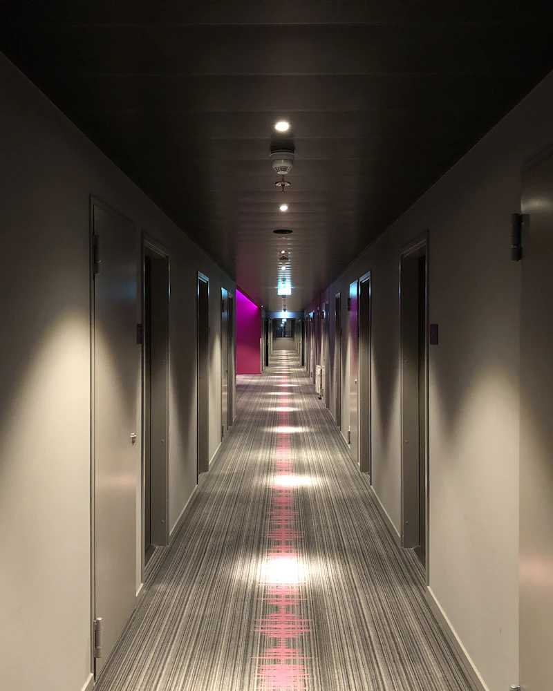 Softly lit hotel corridor with dark walls and a long line of room doors