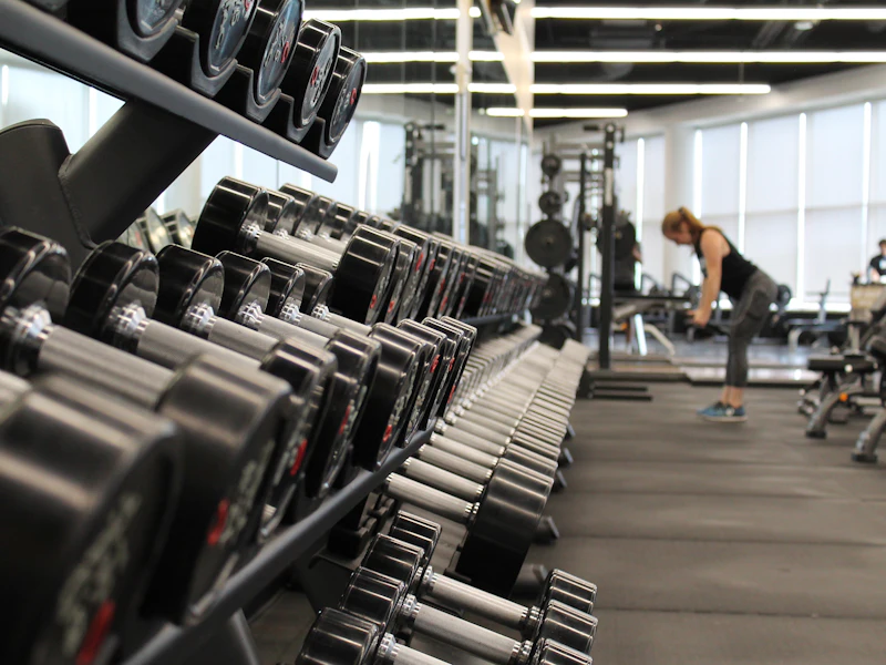 Fitness room with a rack of dumbbells in the foreground and cardio machines by the windows