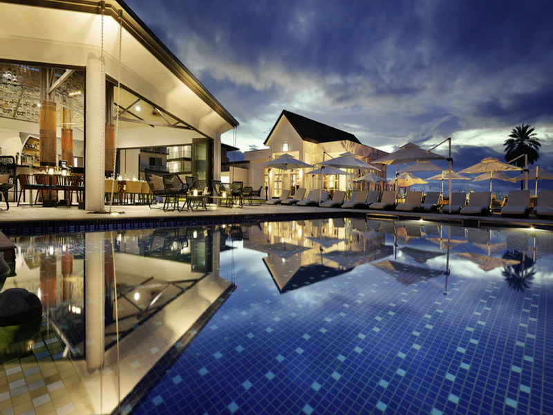 Outdoor hotel pool at dusk reflecting the lit building and palm trees
