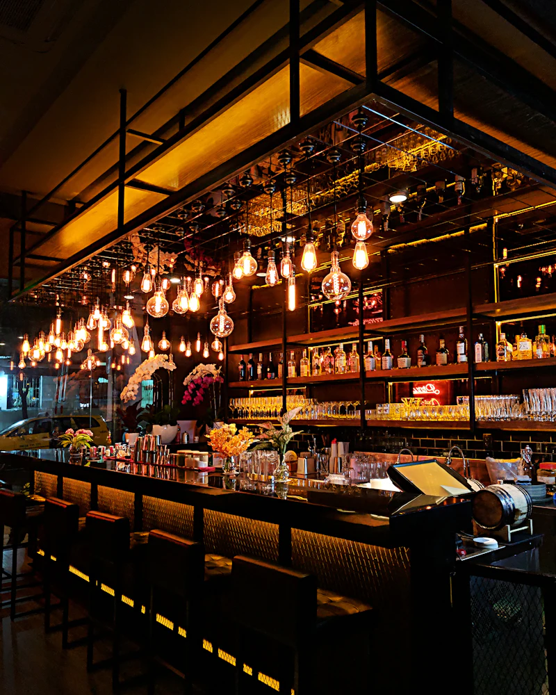 Evening bar with glowing filament bulbs hanging above shelves of bottles