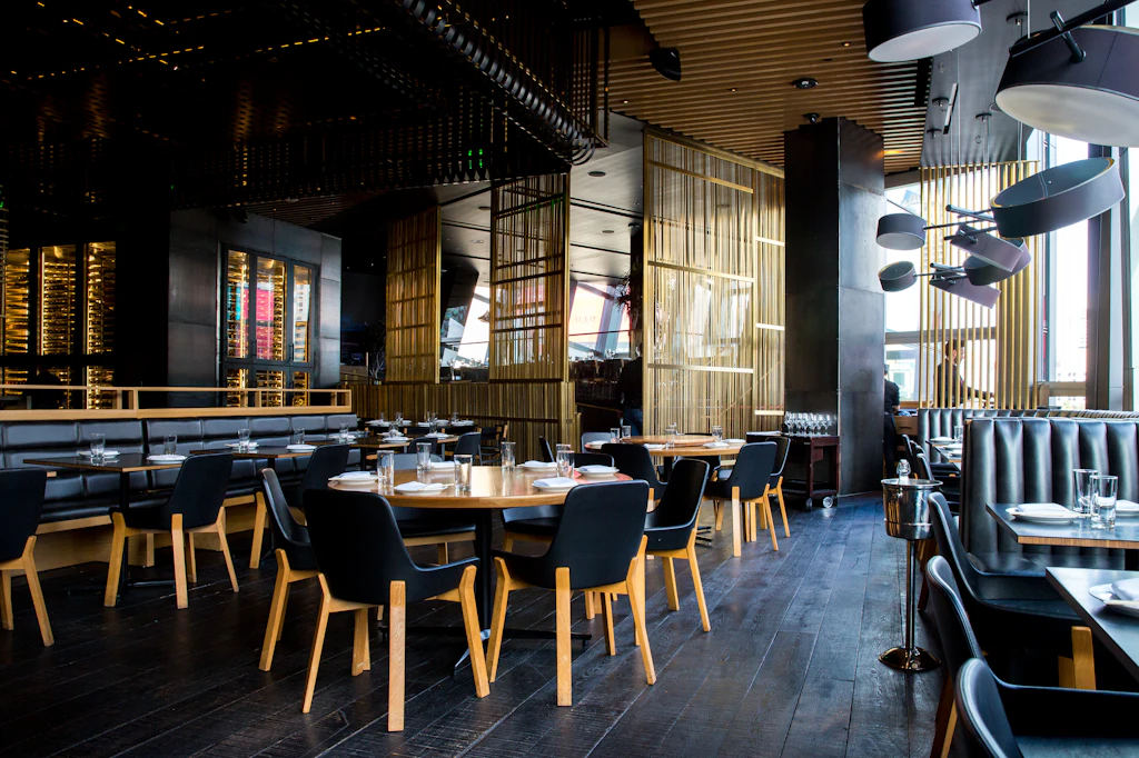 Dimly lit restaurant with dark wood tables, pendant lights and a long banquette