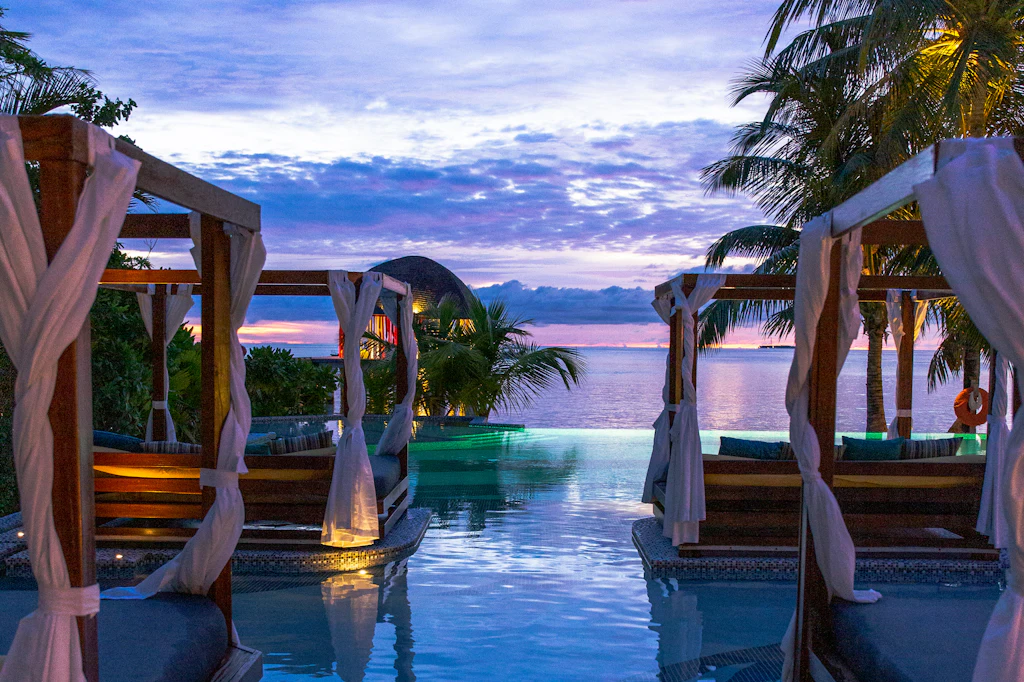 Poolside cabanas with white curtains framing the water at sunset