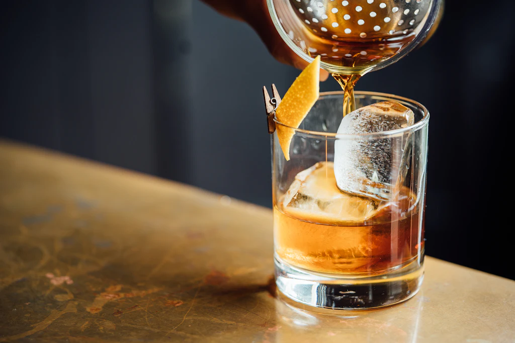 Amber drink being poured over ice into a crystal glass