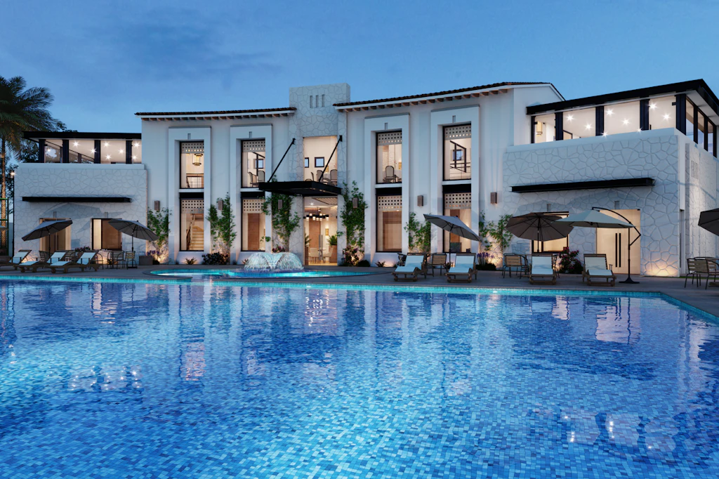 White hotel building at dusk with lit windows reflected in a long pool