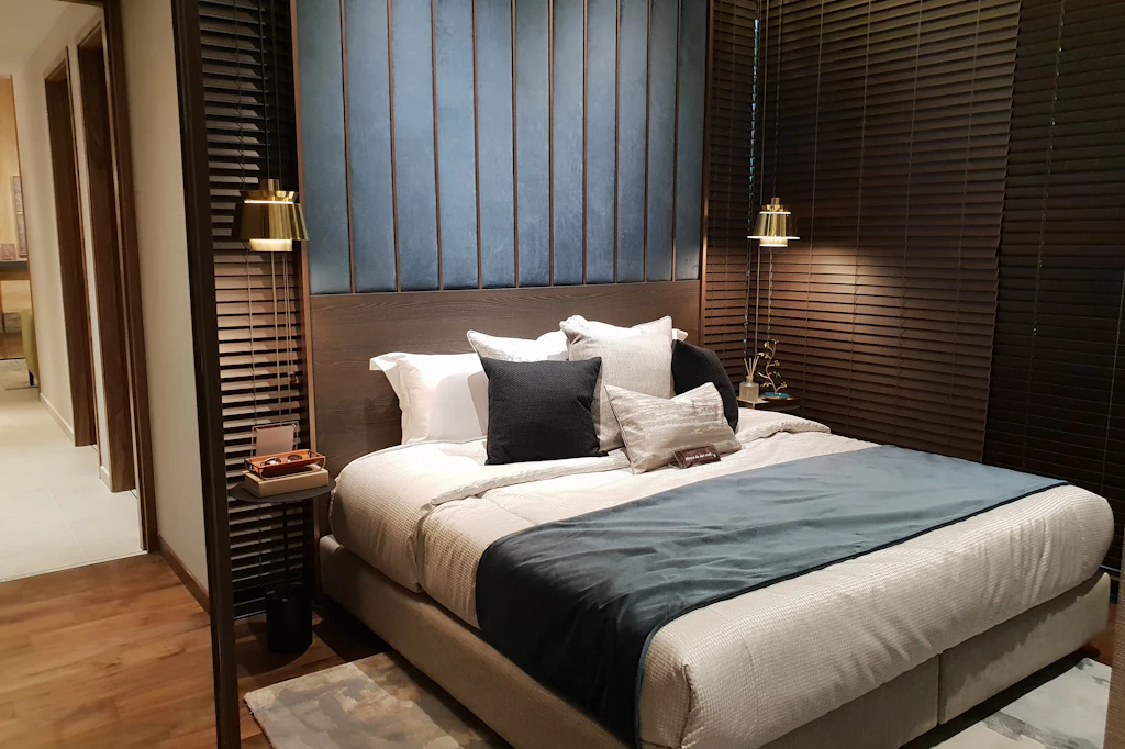 Dimly lit guest room with a made bed, a dark throw and warm wall lights