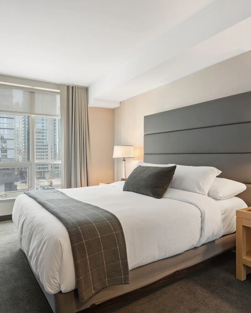 Bright hotel room with a made-up double bed, grey headboard and bedside lamps